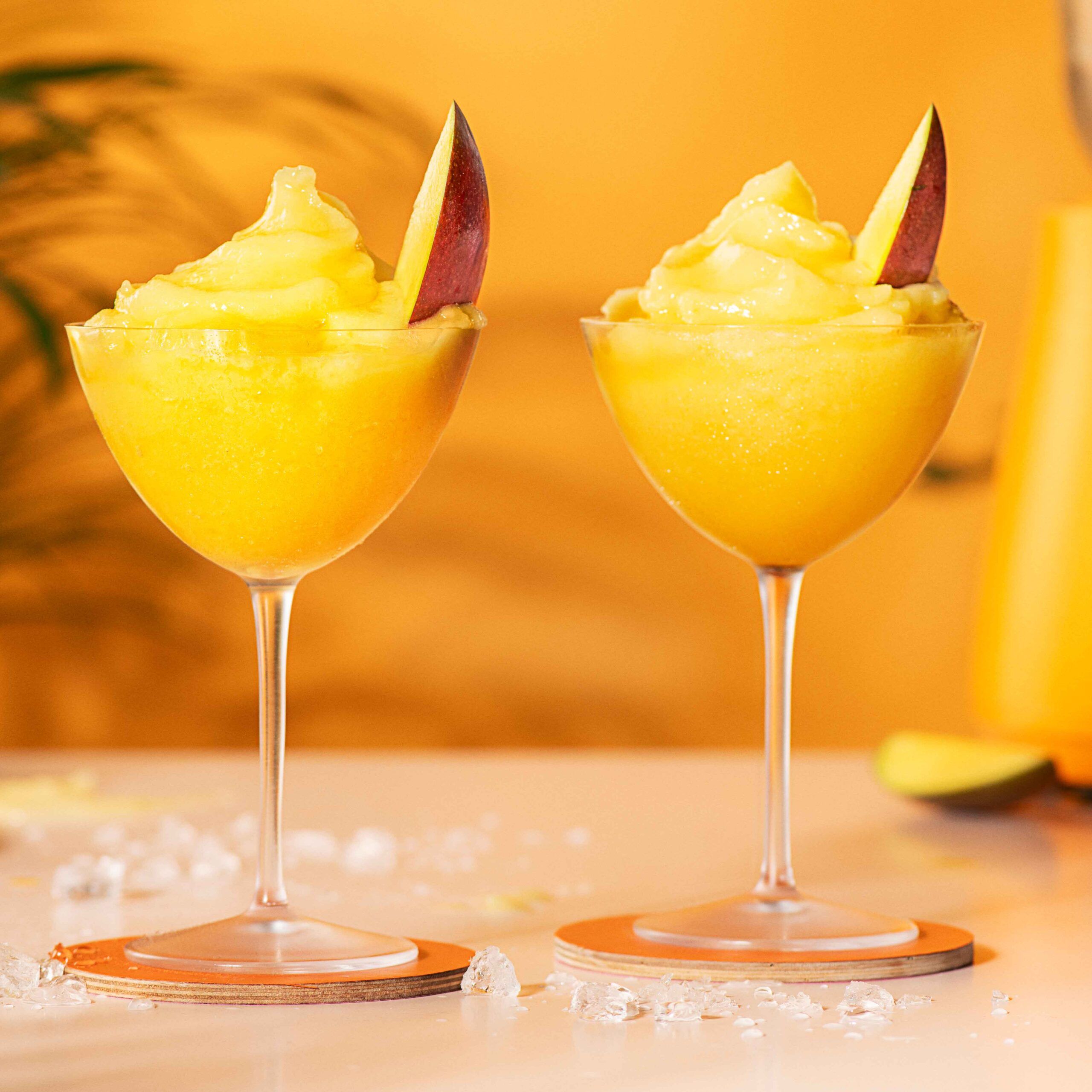 Two frozen mango daiquiris placed on two orange coasters
