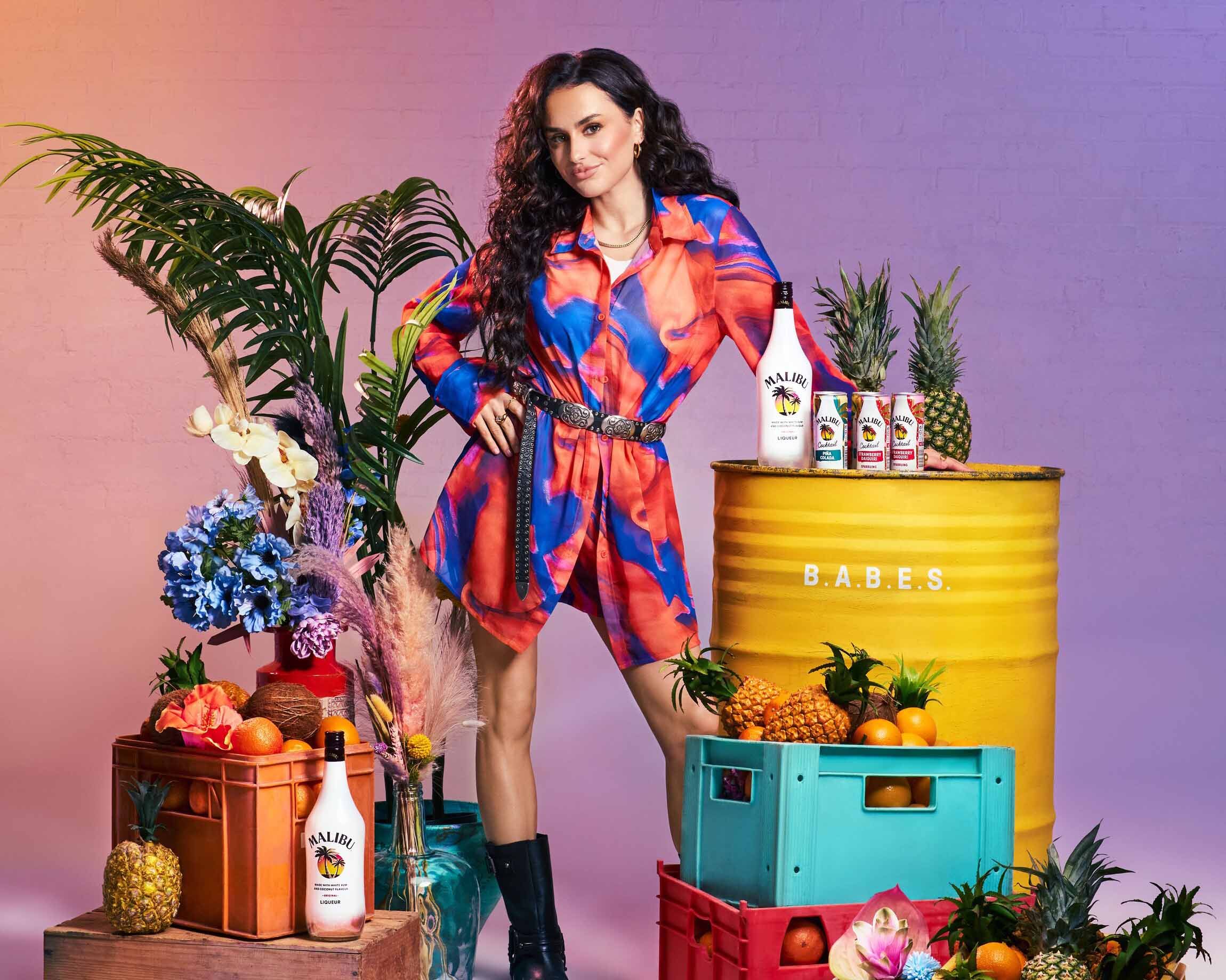 A girl standing by a B.A.B.E.S. barrel with Malibu Original, Malibu cans - pina colada and strawberry daiquiri cocktails