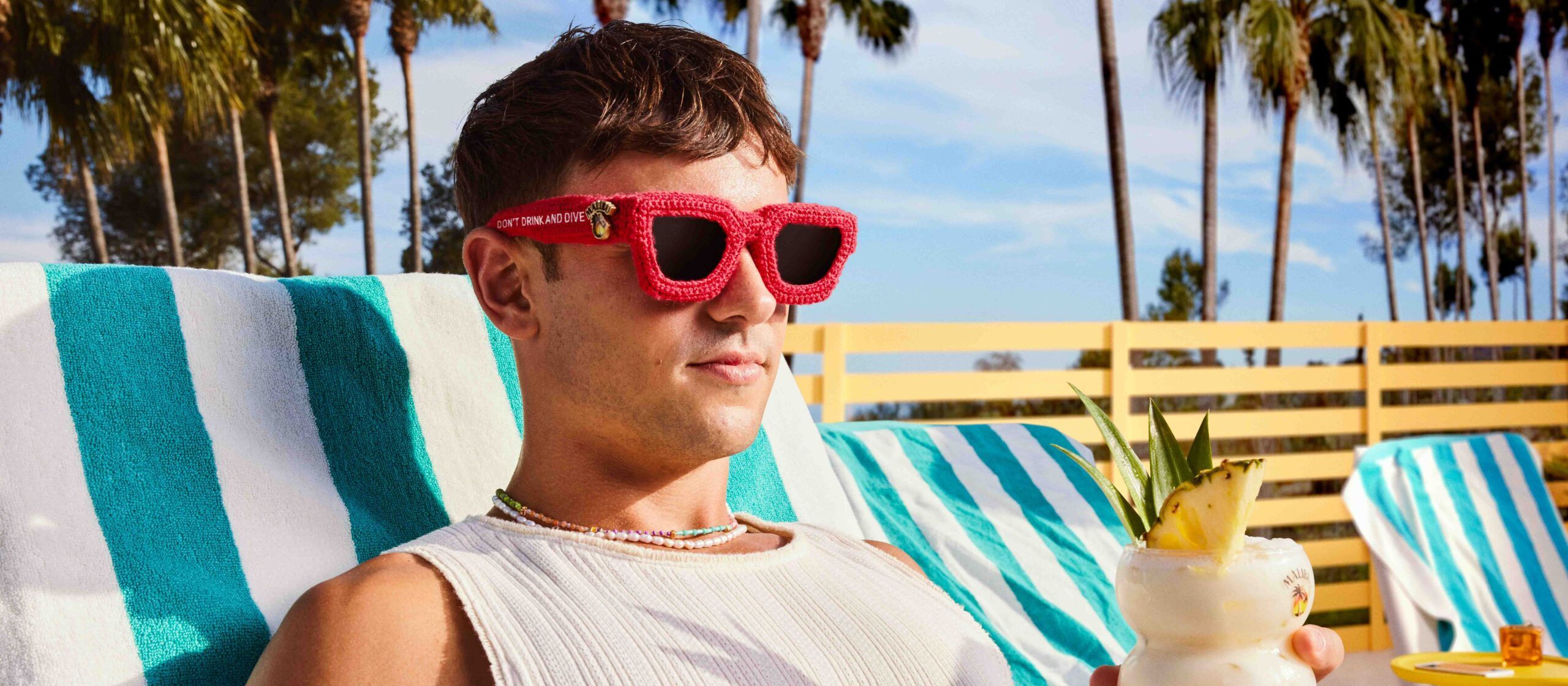 Tom Daley holding a Malibu Pina colada cocktail on a beach