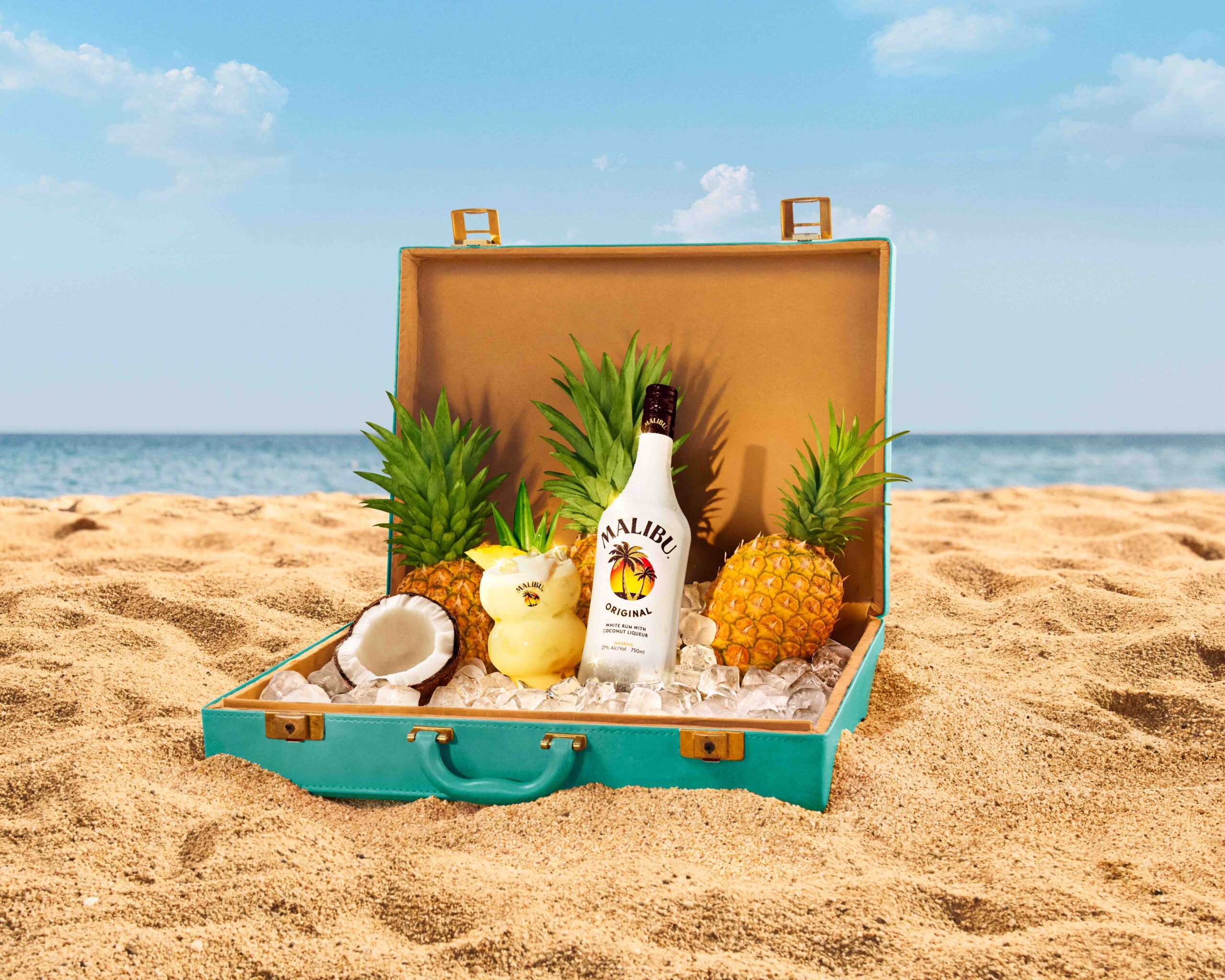 Malibu Pina Colada, bottle and pineapple in open briefcase on beach