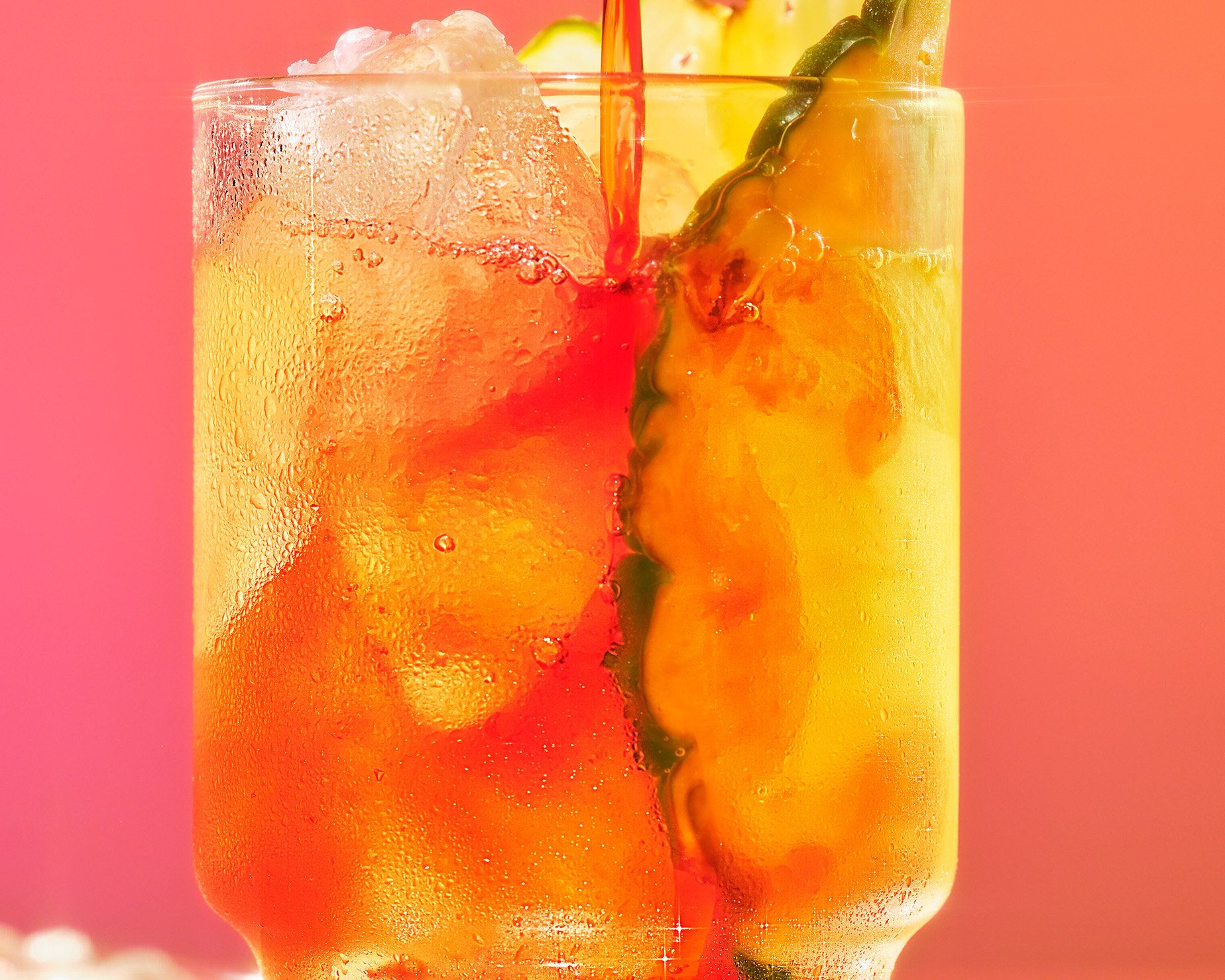 close up of bay breeze with pineapple slice garnish in front of orange background