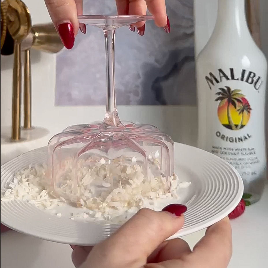 Glass being dipped upside down into plate of coconut shavings