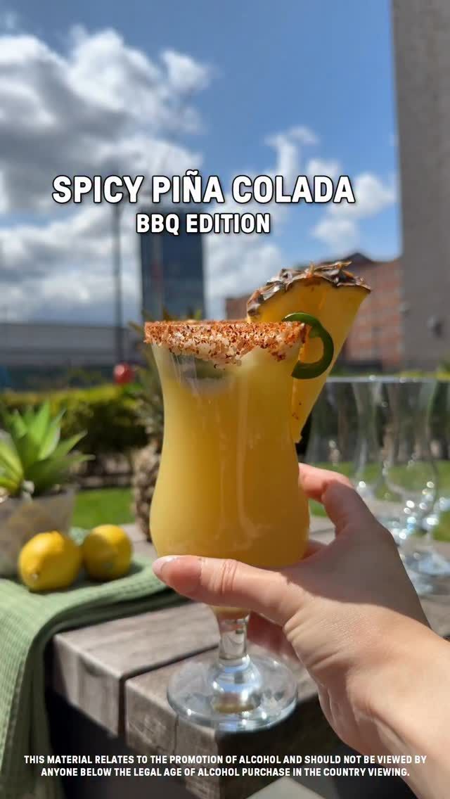 Hand holding a spicy piña colada with chili rim, jalapeño, and pineapple garnish. Text reads: 'Spicy Piña Colada BBQ Edition'.
