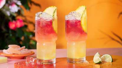 Two Malibu Bay Breeze cocktails served in highball glasses with a pineapple slice standing on a orange tray