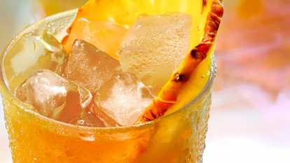 One Malibu Black Bahama Mama cocktail in a hurricane glass garnished with a pineapple wedge served with ice