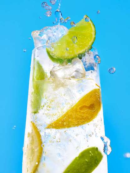 A clear glass of Malibu drink garnished with fresh lime and lemon slices, against a blue background