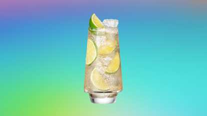 A tall glass of Malibu & Ginger Ale filled with ice and lime slices, topped with a lime wedge. The drink sparkles against a smooth gradient background shifting from purple to turquoise and green, evoking a crisp, refreshing summer vibe.