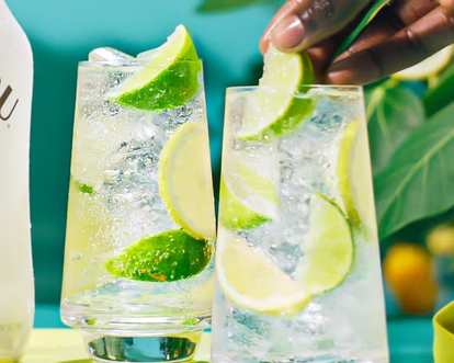 A hand putting a slice of lime in one of two glasses of Malibu Lemonade