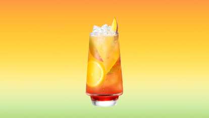 A tall glass of Malibu Mango Sunrise filled with ice cubes, orange slices, and mango wedges, with a hint of red grenadine at the base. The layered coconut rum cocktail glistens with condensation against a warm orange-to-yellow gradient background, evoking a radiant tropical sunrise and a refreshing summer vibe.