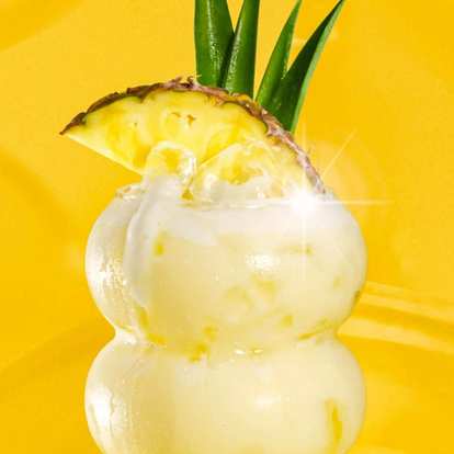 Malibu Piña Colada cocktail in curvy glass with creamy yellow drink, ice, pineapple slice, and green leaves garnish, glowing against a vibrant yellow background.