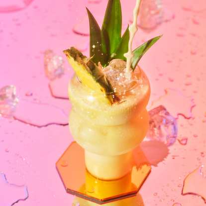 Malibu Piña Colada cocktail standing on a pink table served in a hurricane glass and a pineapple wedge