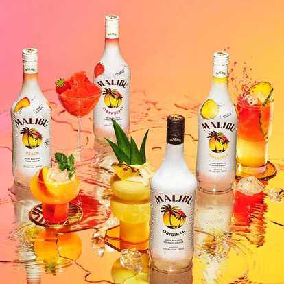 Malibu Original, Peach, Strawberry, and Pineapple bottles with colorful cocktails, ice, and fruit garnishes on reflective surface, warm gradient background creating tropical summer atmosphere.