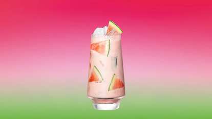 Malibu Watermelon Colada — a creamy pink cocktail served in a tall glass with ice and watermelon slices, topped with a wedge of watermelon against a pink‑to‑green gradient background.