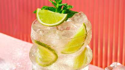 Malibu Spritz — a chilled cocktail with ice, lime slices, and mint leaves in a clear glass, topped with fresh mint and lime wedges against a warm pink background for a bright, refreshing look.