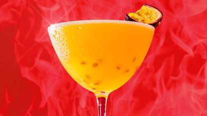 Malibu Passion Fruit Daiquiri cocktail in a coupe glass with bright golden drink, frothy top, and halved passion fruit garnish, glowing against a vivid red background with soft mist.