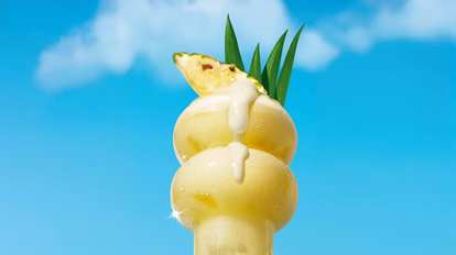 A Pina colada decorated with pineapple on a blue background with clouds