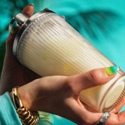 Two hands shaking a pina colada in a glass shaker