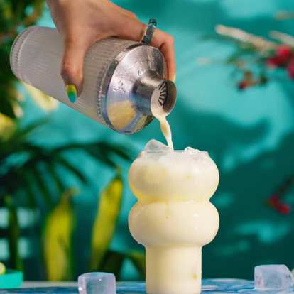 A hand pouring Pina Colada from a shaker into a glass