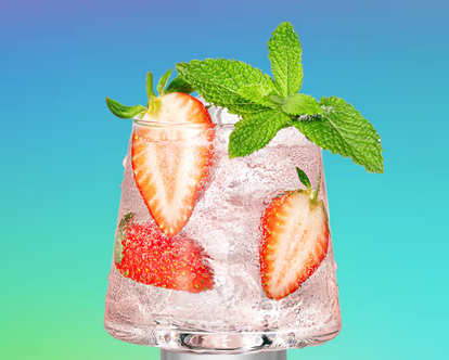 Malibu Rosé Spritz in a short glass with clear sparkling drink, ice cubes, sliced strawberries, and fresh mint leaves, set against a blue‑to‑green gradient background.