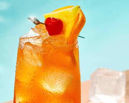 An orange tropical Malibu drink with ice and tropical fruits